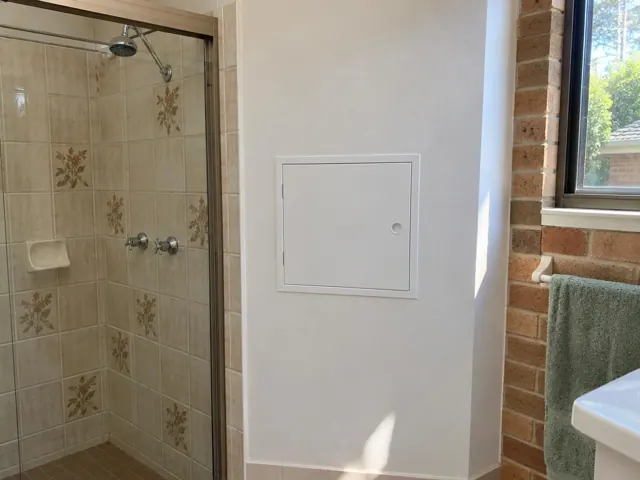 White access panel in a bathroom wall beside a tiled shower in Frenchs Forest